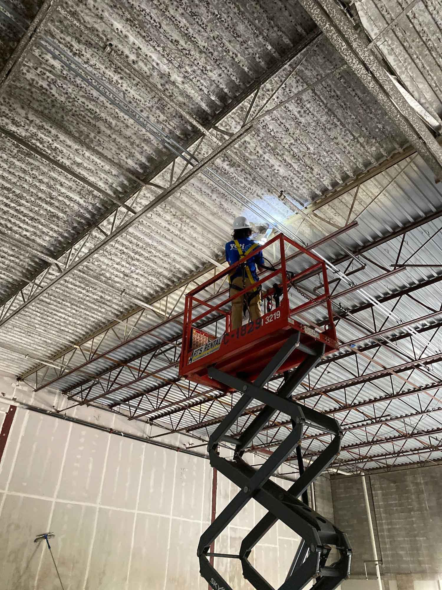 Yeti Restoration technician on a scissor lift dry ice blasting a corrugated metal ceiling deck