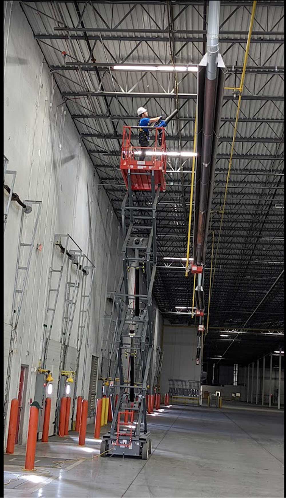 Yeti Restoration technician on a scissor lift dry ice blasting overhead pipework in a warehouse