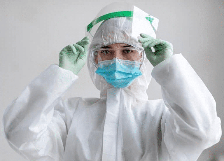 Person in a white protective suit, face mask and face shield adjusting their hood