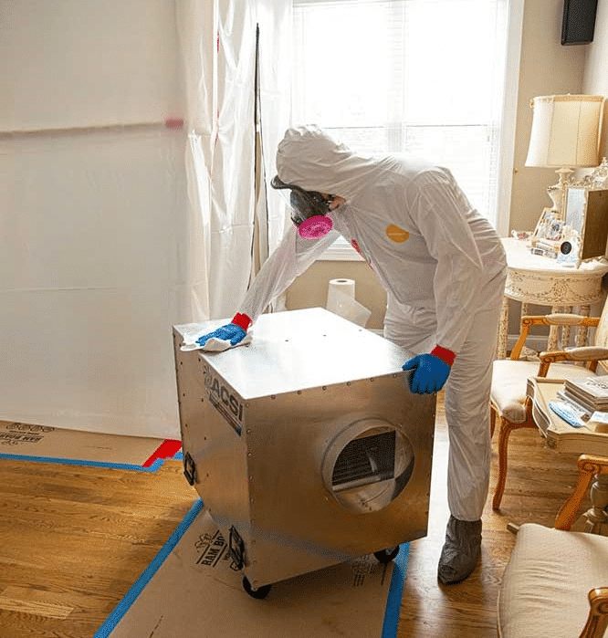 Technician in protective gear positioning an air scrubber in a room